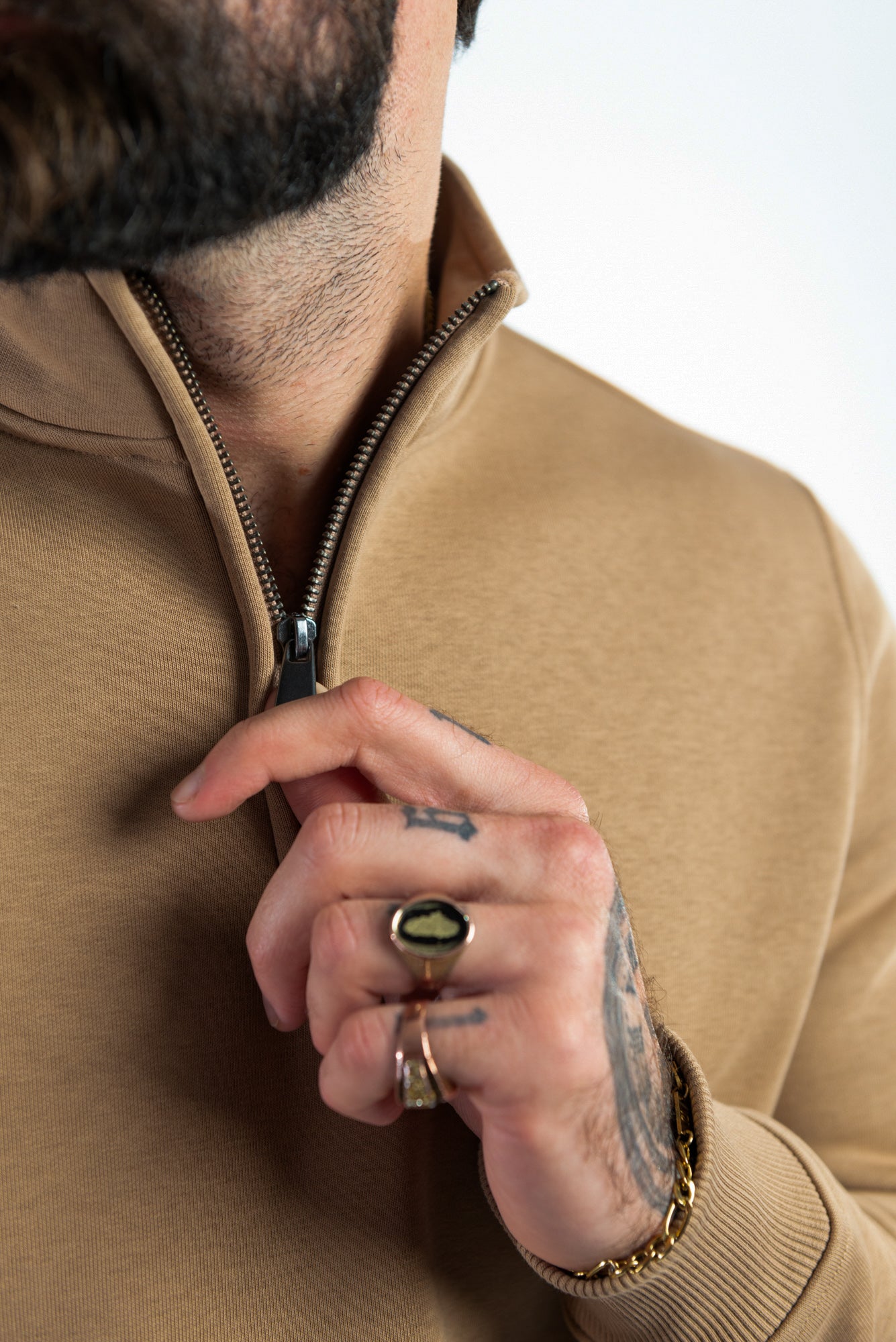 A man unzipping a organic cotton 1/4 zip jumper in hazelnut, by Pioneer Clothing. 