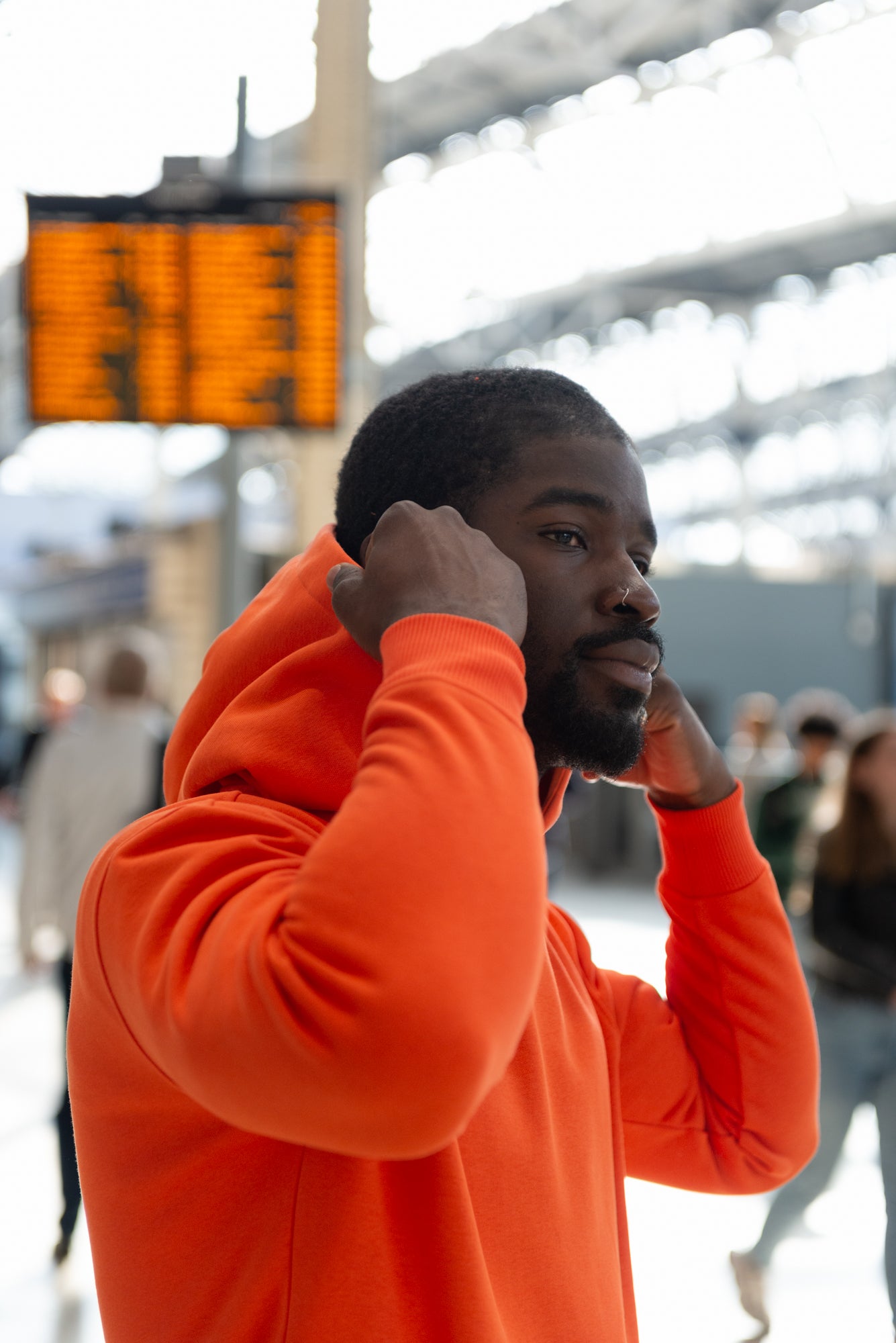 A man  in the tube station wearing a mandarin orange, organic cotton hoodie by Pioneer Clothing 