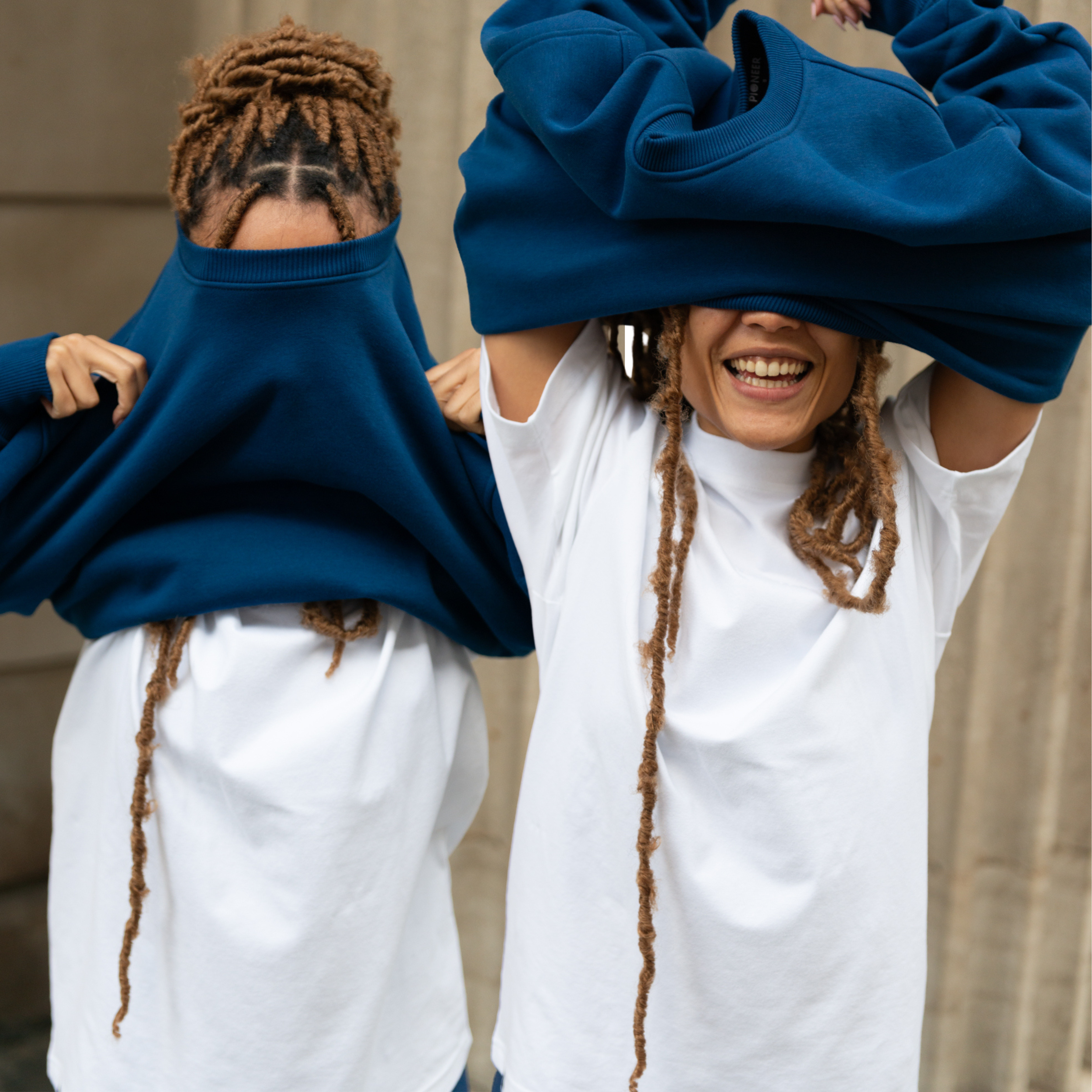 Woman  wearing white organic cotton t-shirt pulling a navy organic cotton crew neck over her head. 