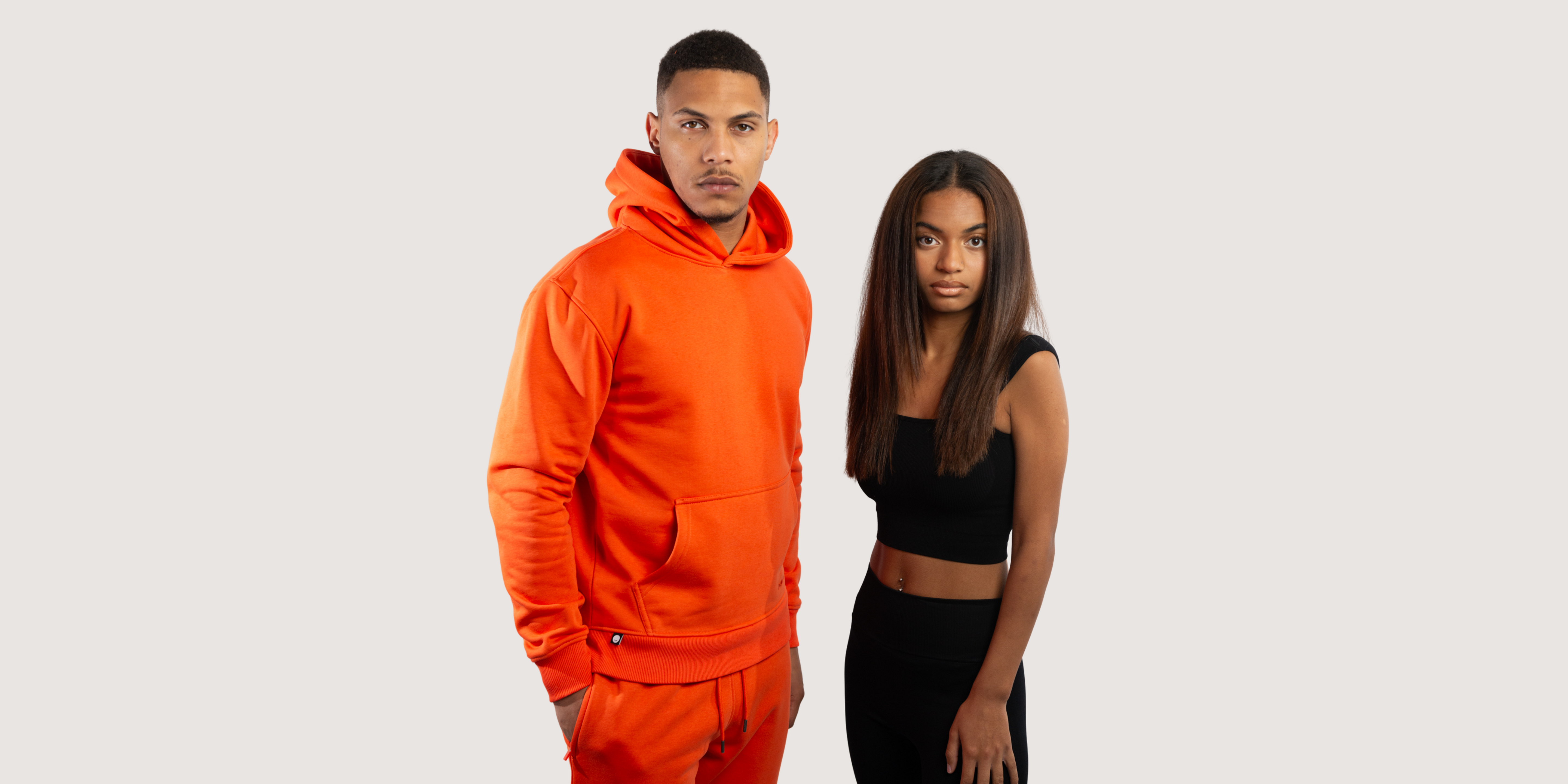 Two model facing front. Male model wearing Mandarin Red Hoodie and Joggers and Female model wearing Black Seamless Vest Top and Leggings.