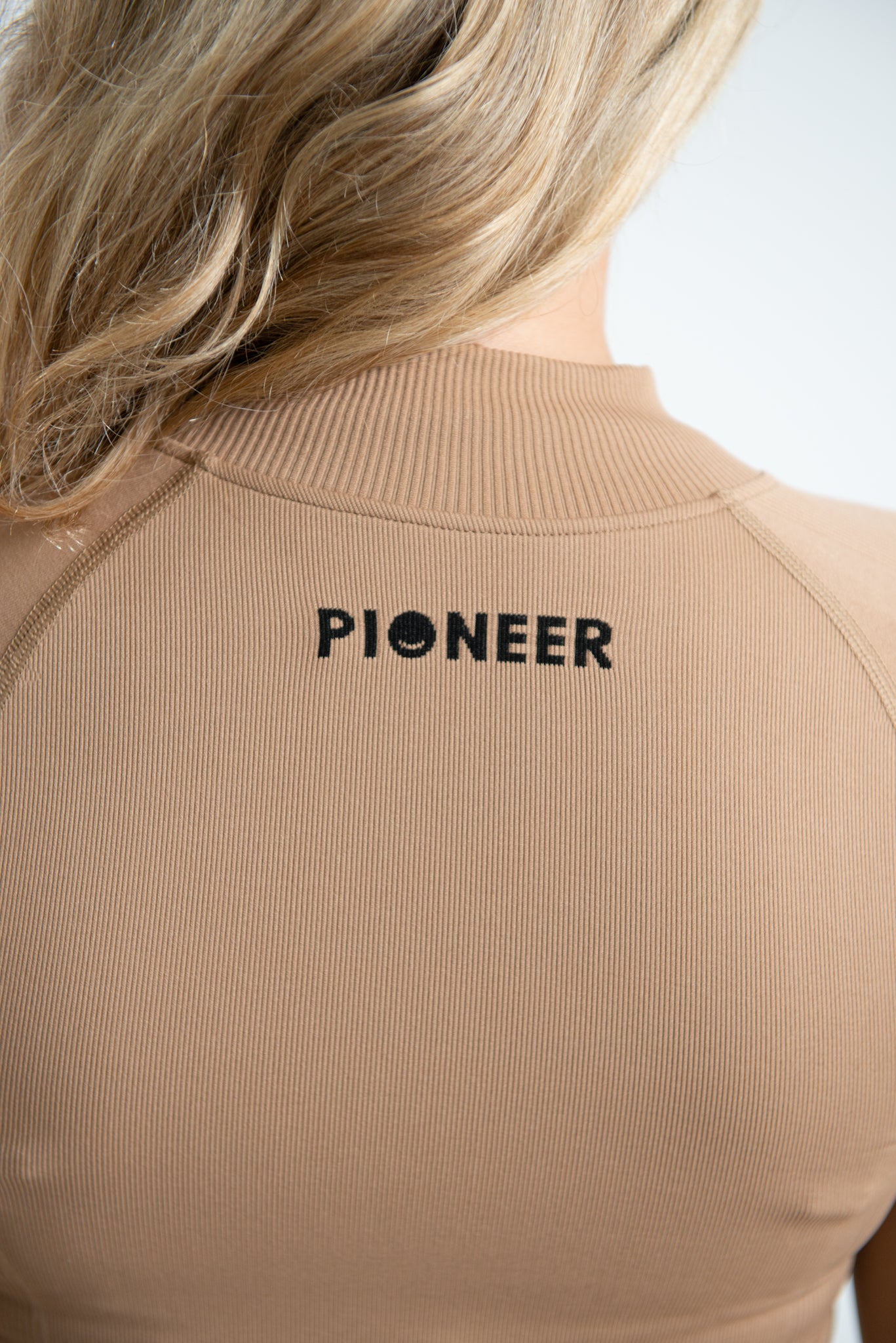 A close-up image of the back woman wearing a form fitted zip top. The image is showing the back of the jacket focusing on the Pioneer logo which is located towards the top of the jacket which is made from sustainable eco-friendly materials.