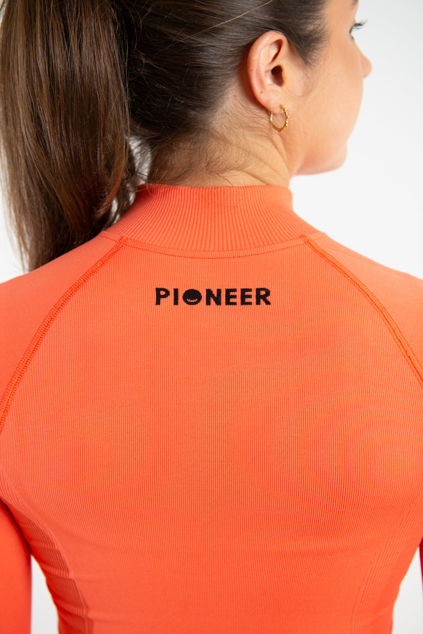 A close-up image of the back woman wearing a form fitted zip top. The image is showing the back of the jacket focusing on the Pioneer logo which is located towards the top of the jacket which is made from sustainable eco-friendly materials.